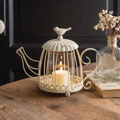 a white teapot with a candle in it sitting on a table next to a book