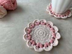 two crocheted coasters sitting on the floor next to a white vase and ball of yarn