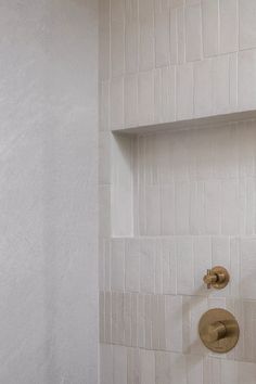 a white tiled shower with gold faucet and hand held shower head in the corner