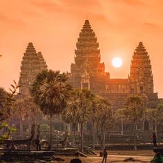 the sun is setting in front of an ancient building with palm trees and people walking around