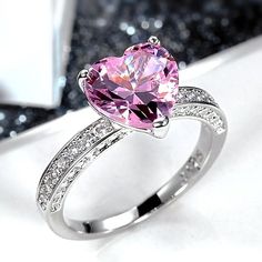 a pink heart shaped ring with diamonds around it