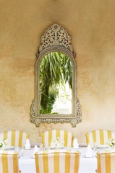 a dining room with yellow striped chairs and a large mirror on the wall above it