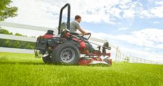 a man riding on the back of a red lawn mower across a lush green field