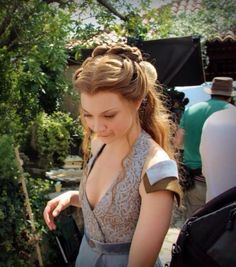 a woman in a dress looking down at something on the ground with other people around her