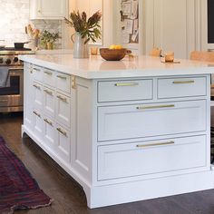 a kitchen island with white cabinets and gold pulls on the drawers, in front of an oven