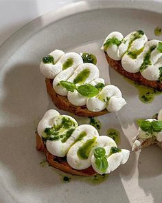 four pieces of bread topped with mozzarella and green sauce on a white plate