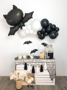 a halloween party with black and white balloons, bats, and other decorations on the table