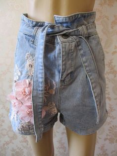 "Stone washed light denim shorts with pink embroidery and pink appliqued flowers on the front.  They have a high waist with a tie belt,  turned up hem, a zip fly and 2 pockets front and back. Waist flat;  30\" Outside leg from waist;  25\" Width of leg;  12\" Made by REAULAR cotton denim" Cute Short Summer Jeans, High Waist Jeans For Summer Festival, Summer Festival High Waist Jeans, Trendy Jean Shorts For Spring Festival, Light Wash Cutoff Jean Shorts For Spring, Denim Shorts For Summer Festival, Cute High Waist Jean Shorts For Spring, Bohemian Style Denim Blue Jeans For Summer, Bohemian Denim Blue Jeans For Summer