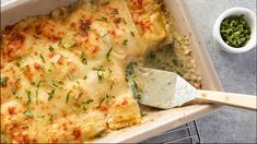 a casserole dish with cheese and herbs in it next to a small bowl of dip