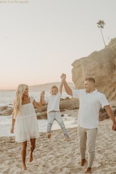 a family running on the beach with their arms in the air and holding hands up