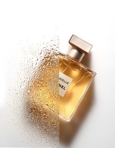 a bottle of perfume sitting on top of a white surface with drops of water around it