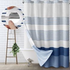 a bathroom with a blue and white striped shower curtain next to a bathtub, potted plant and toilet paper dispenser