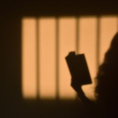 the shadow of a person holding a book in front of a window with bars on it