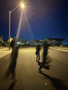 two skateboarders are riding down the street at night with their shadows on the pavement