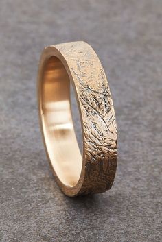 a gold wedding ring with an etched design on the outside and inside, sitting on a gray surface