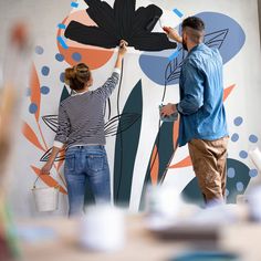 a man and woman painting a mural on the side of a wall in an office