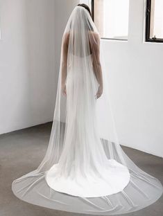 a woman in a white wedding dress with a veil on her head is looking down at the floor