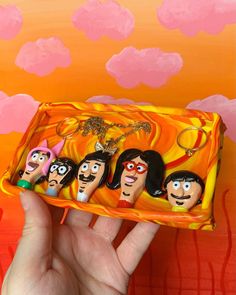 a hand holding an orange and yellow box with cartoon characters painted on the inside, in front of a colorful background