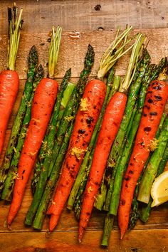 asparagus, carrots and lemon slices on a wooden board with herbs sprinkled all over them