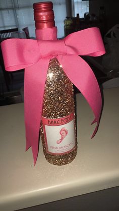 a bottle that is sitting on a table with a pink ribbon around it and some glitter