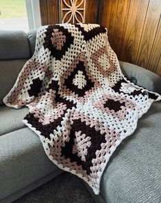 a crocheted blanket sitting on top of a couch in front of a window