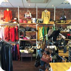 a clothing store filled with lots of clothes and handbags on shelves next to a brick wall