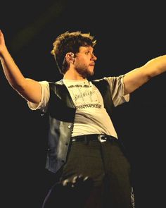 a man holding his arms out in the air while wearing a vest and black pants