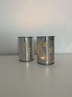 two tin canisters sitting on top of a white table next to each other