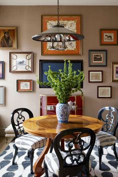 a dining room table with chairs and pictures on the wall behind it, along with a potted plant