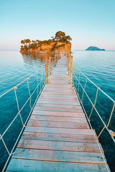 a wooden dock leading to an island in the middle of the ocean with rope railings