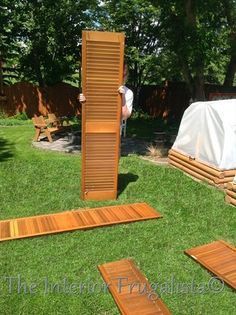 a man standing next to a wooden door in the grass with several pieces of wood laid out on it