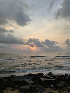 the sun is setting over the ocean with rocks on the shore and waves coming in