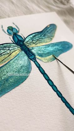 a blue dragonfly sitting on top of a piece of paper