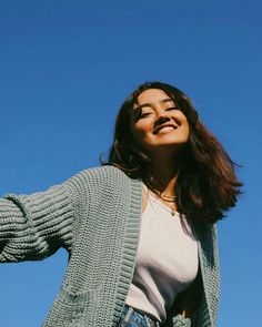 a woman standing in front of a blue sky and holding her arms out to the side