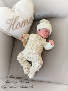 a baby laying on top of a gray couch next to a pillow with the word home written on it