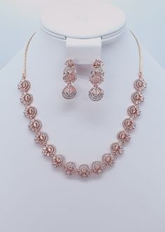 "This necklace set features a beautiful circular floral pattern that makes it a perfect accessory for the festive season. Pair it with the perfect wedding ceremony dress or an ethnic piece specially made for big occasions! Neckline Length: 9.5\" and The length of the necklace is adjustable by a chain. Earrings Length: Approx. 1.5\" Rose Gold finish on high-quality brass as the base metal Availability: In-Stock *Color may vary slightly due to light condition & photography. Jewelry Care:  Keep away from moisture. Allow perfumes and lotion to dry before wearing. Store in jewelry pouch. Clean only with soft lint free cloth" Festive Cubic Zirconia Jewelry Sets, Rose Gold Round Jewelry Sets For Weddings, Hand Set Rose Gold Bridal Necklace For Reception, Festive Cubic Zirconia Bridal Sets, Festive Round Cubic Zirconia Bridal Sets, Hand Set Rose Gold Jewelry Sets, Rose Gold Hand-set Round Jewelry Sets, Gold Necklace Set Bridal, Wedding Ceremony Dress