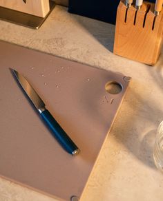 a knife is laying on top of a cutting board next to a glass and wooden block