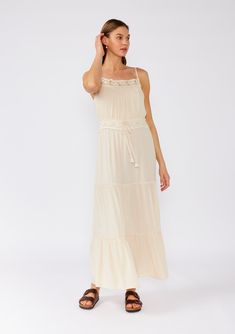 [Color: Natural] A front facing image of a brunette model wearing an off white sleeveless maxi dress. With adjustable spaghetti straps Spring Tiered Maxi Dress With Lace Trim, Summer Maxi Dress With Lace Trim And Tiered Skirt, Summer Tiered Maxi Dress In Rayon, Summer Rayon Tiered Maxi Dress, Beach Tiered Skirt Maxi Dress In Rayon, Bohemian Rayon Maxi Dress With Spaghetti Straps, Bohemian Tiered Dress With Adjustable Straps, Bohemian Dress With Adjustable Straps And Tiered Design, Casual Maxi Dress With Lace Trim