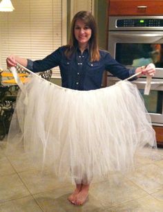 a woman is holding up a white tulle skirt while standing in front of an oven