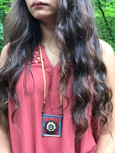 a woman with long dark hair wearing a red top and brown beaded necklace is standing in front of some trees