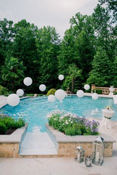 an outdoor swimming pool with white balloons floating in the air and flowers on the ground