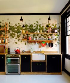 a kitchen with black cabinets and green geometric tiles on the wall behind the stove top