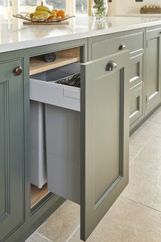 a kitchen with green cabinets and an open trash can on the counter top, in front of a window