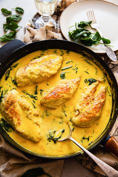 a pan filled with chicken and spinach covered in yellow sauce on top of a table