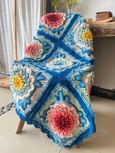 a crocheted blanket is sitting on a wooden stand next to a potted plant