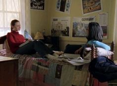 two women sitting on top of a bed in a room with posters hanging above them