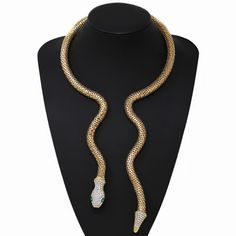 Elevate your style with the Serpentine Crystal Necklace Set. This stunning piece features a striking serpentine design, resembling a snake coiled elegantly around your neck. Crafted from high-quality, shimmering crystals, this necklace radiates luxury and sophistication. The intricate details of the snake's head and tail, adorned with green gem-like stones for the eyes, add a realistic and exotic touch. Designed to fit snugly and comfortably, this choker makes a bold fashion statement, perfect f Gold Snake-shaped Jewelry For Party, Elegant Adjustable Snake Shape Necklaces, Elegant Adjustable Snake Shape Necklace, Gold Snake-shaped Party Jewelry, Elegant Snake-shaped Metal Jewelry, Elegant Snake Shape Necklace For Party, Snake Coiled, Serpentine Crystal, Necklace Set Gold