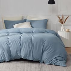 a bed with blue comforters and pillows in a white room next to a lamp