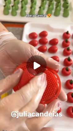 a person holding a red object in front of small tomatoes on a tray with plastic caps