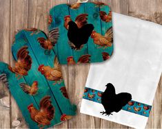 two oven mitts with roosters on them, one is blue and the other is white